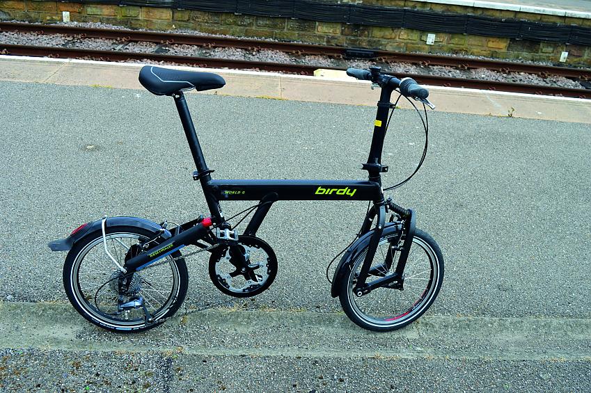 A black Birdy folding bicycle propped up on a railway platform
