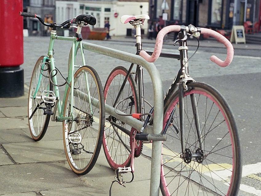 Two bikes, one pink and one turquoise, locked to a metal cycle stand