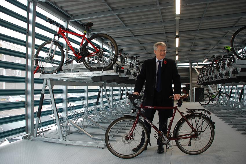 A man is standing with a red Surly touring bike in a cycle parking hub with several bikes in the parking areas