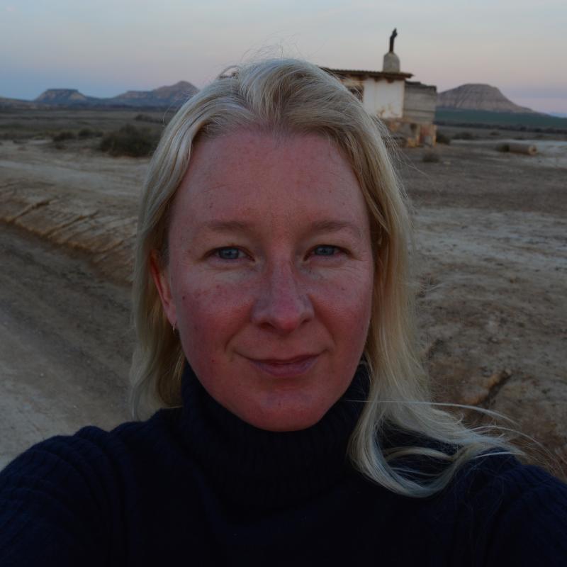 Close-up headshot of Anna in a desert landscape. She is wearing a dark jumper. 