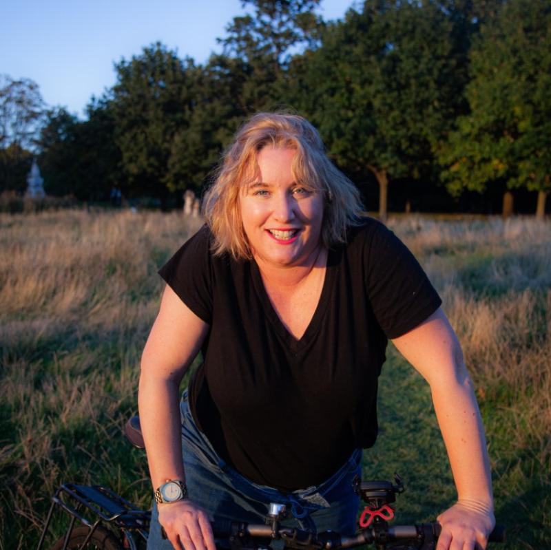 Carla is facing the camera with her bike in a park. She is wearing black T-shirt and jeans. Photo: Graham Berry.