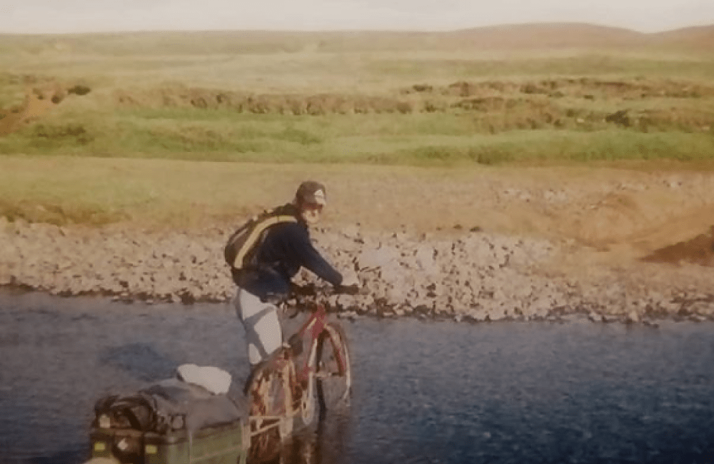 A cyclist crosses an Icelandic river with a cycle trailer