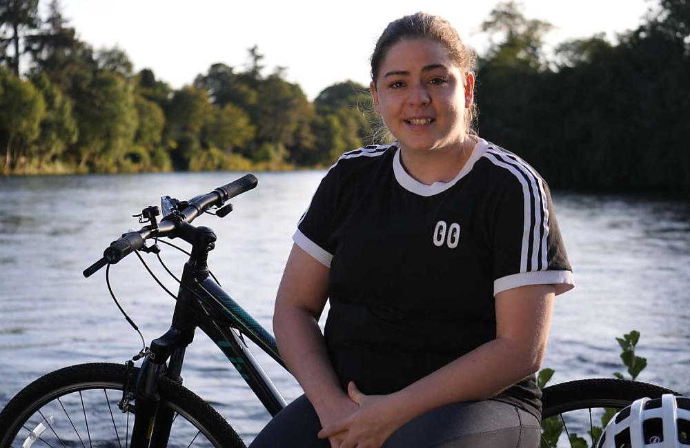 A young woman sat by a lake with her bicycle 
