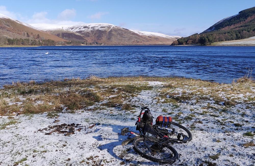 Bike resting in the snow in front of a loch